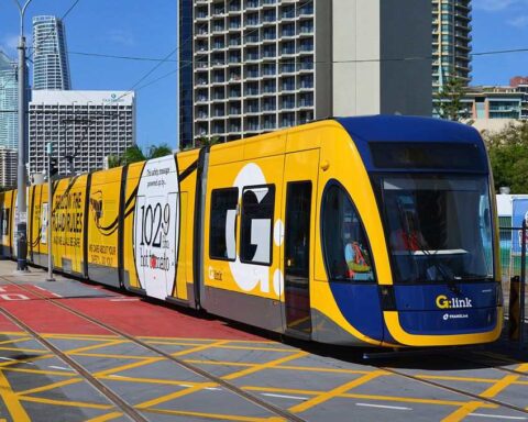 Yellow and blue G:link tram operating on the Gold Coast Light Rail system traveling through Surfers Paradise with high-rise buildings in the background.