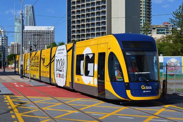 Yellow and blue G:link tram operating on the Gold Coast Light Rail system traveling through Surfers Paradise with high-rise buildings in the background.