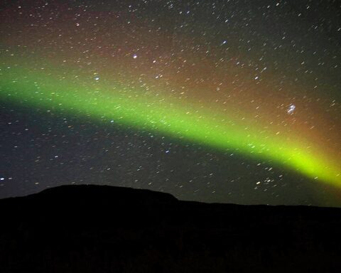 Northern Lights display showing a vivid green aurora arc against the dark night sky with stars visible in the background.