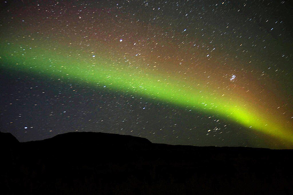 Northern Lights display showing a vivid green aurora arc against the dark night sky with stars visible in the background.