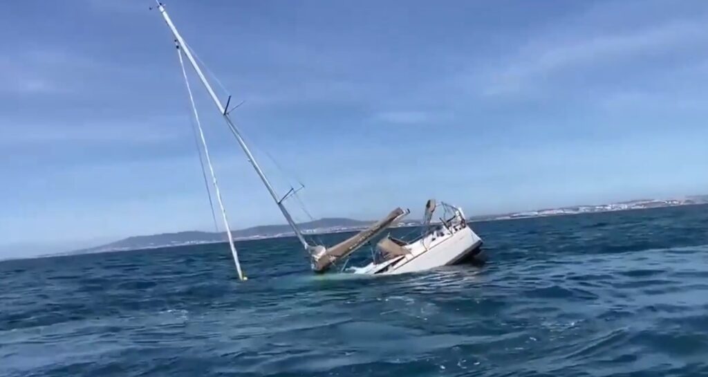 Sinking sailing yacht off the coast of Portugal after orca encounter, mast leaning into the water.
