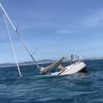 Sinking sailing yacht off the coast of Portugal after orca encounter, mast leaning into the water.