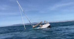 Sinking sailing yacht off the coast of Portugal after orca encounter, mast leaning into the water.
