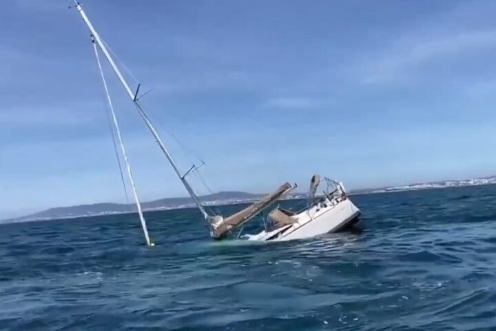 Sinking sailing yacht off the coast of Portugal after orca encounter, mast leaning into the water.
