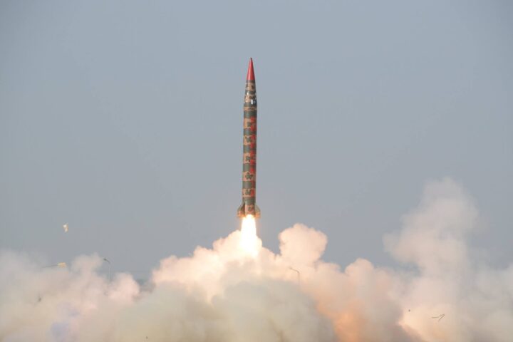Rocket launching with bright orange flames and white exhaust plumes against cloudy sky during liftoff