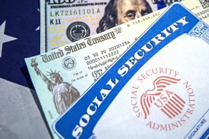 Close-up of a Social Security card, U.S. Treasury check, and U.S. currency placed over part of the American flag, symbolizing Social Security payments and federal benefits.