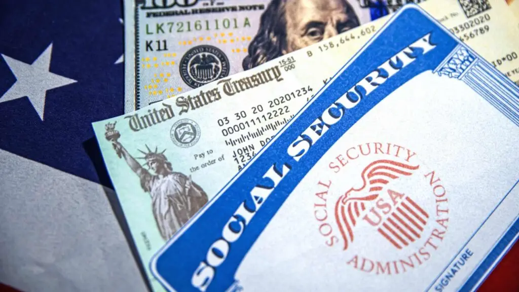 Close-up of a Social Security card, U.S. Treasury check, and U.S. currency placed over part of the American flag, symbolizing Social Security payments and federal benefits.