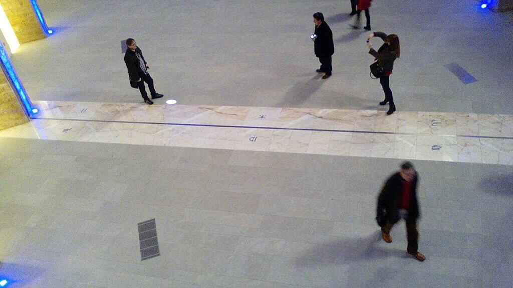 Security camera footage showing several people walking through an indoor corridor, likely seeking relief from extreme outdoor temperatures.