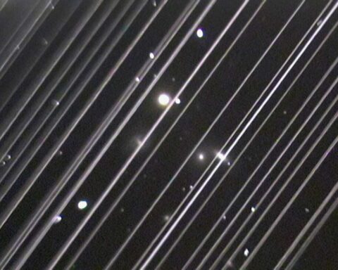 Long‑exposure photograph of the night sky showing diagonal bright trails from passing Starlink satellites against a backdrop of stars and the NGC 5353/4 galaxy group.