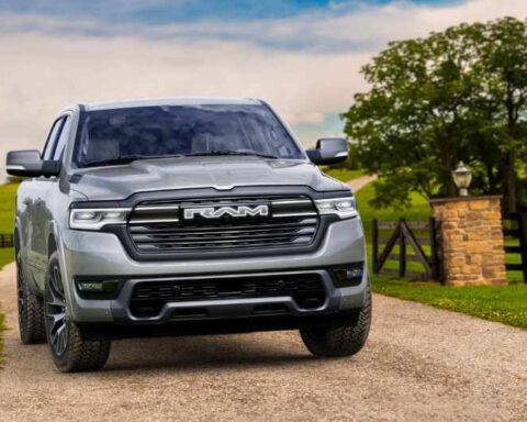 2026 Ram 1500 REV pickup truck in silver, shown driving on a highway with desert landscape in the background.
