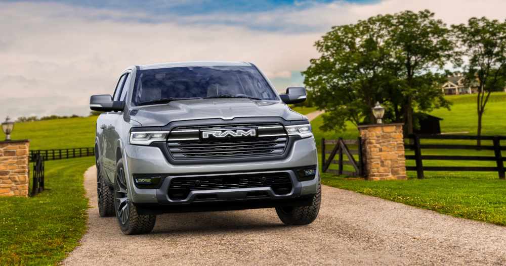 2026 Ram 1500 REV pickup truck in silver, shown driving on a highway with desert landscape in the background.