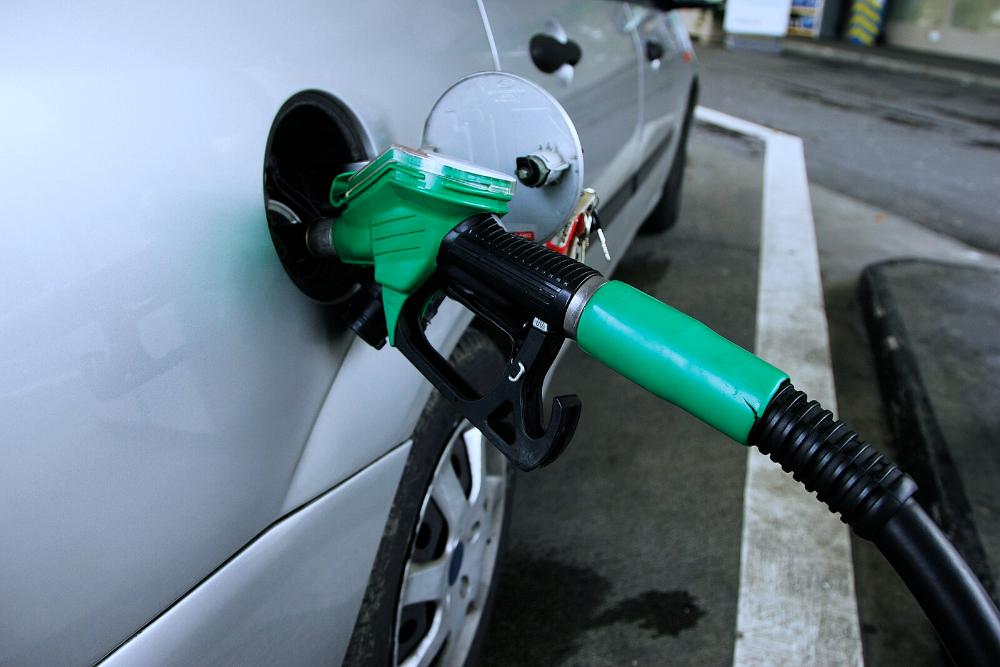 Green petrol pump nozzle inserted into the fuel tank of a white car at a gas station, highlighting fuel delivery system relevant to E20 ethanol blending discussions