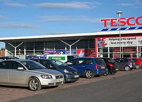 Exterior of a Tesco supermarket with red logo signage and cars parked in the foreground.