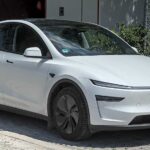 White Tesla Model Y electric vehicle parked in an outdoor setting, showcasing the compact SUV design that Tesla is using for its robotaxi testing program.