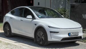 White Tesla Model Y electric vehicle parked in an outdoor setting, showcasing the compact SUV design that Tesla is using for its robotaxi testing program.