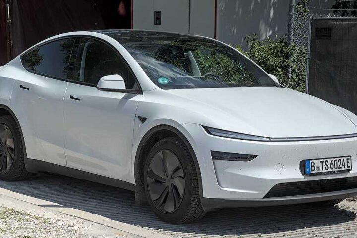White Tesla Model Y electric vehicle parked in an outdoor setting, showcasing the compact SUV design that Tesla is using for its robotaxi testing program.