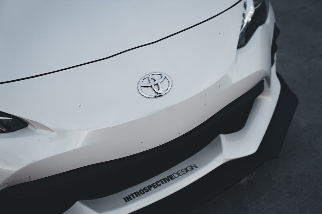 Close-up of a white Toyota vehicle showing the Toyota logo on the front bumper with "INTROSPECTIVEDESIGN" text visible on the lower portion