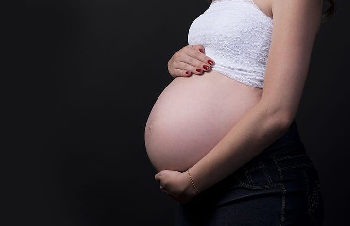 Side profile of a pregnant woman in a white crop top holding her belly against a black background