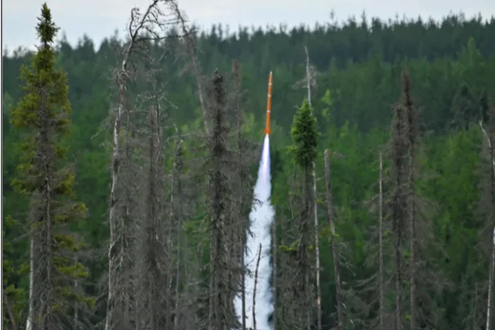 Orange Spectre rocket launched by Turner Fenton Secondary School students streaking upward through a forest clearing at Launch Canada 2025 in Timmins, Ontario.