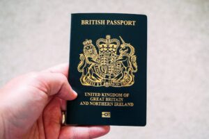 Hand holding a dark blue British passport with gold emblem and text reading "United Kingdom of Great Britain and Northern Ireland"