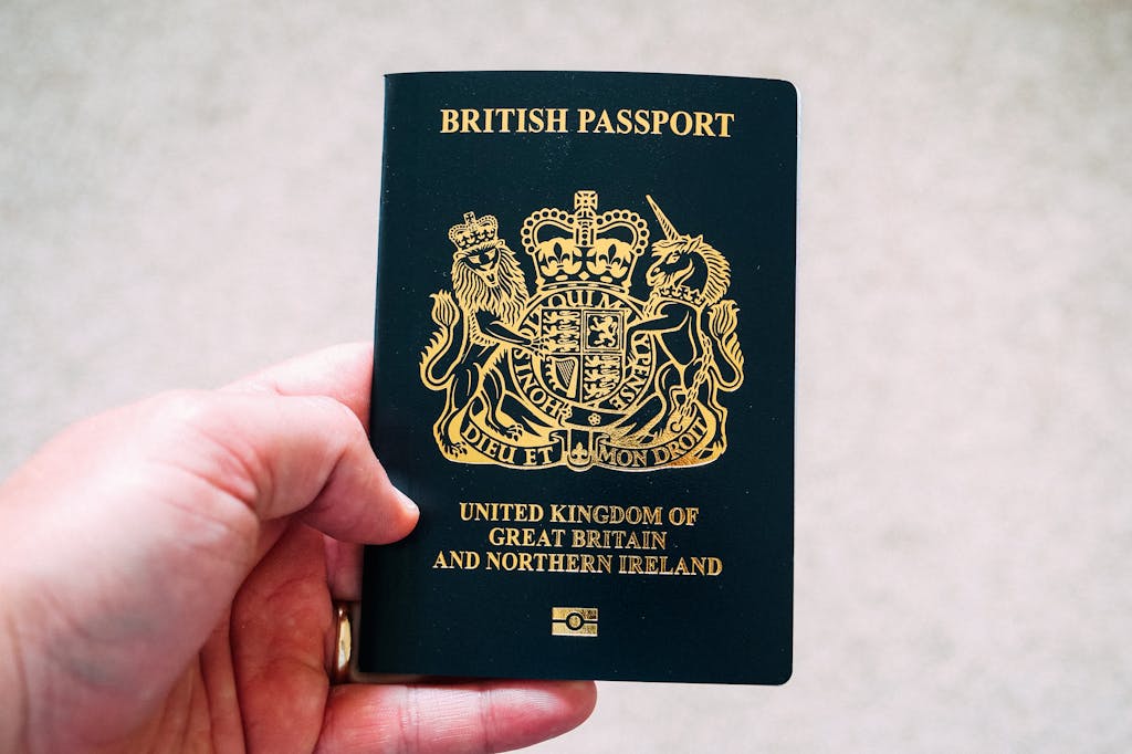 Hand holding a dark blue British passport with gold emblem and text reading "United Kingdom of Great Britain and Northern Ireland"