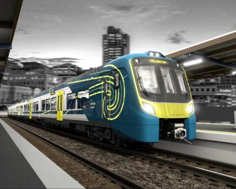 Modern blue and yellow Adessia Stream B battery-electric train with distinctive streamlined design at a station platform at night, showing the front cab and passenger cars with illuminated interior