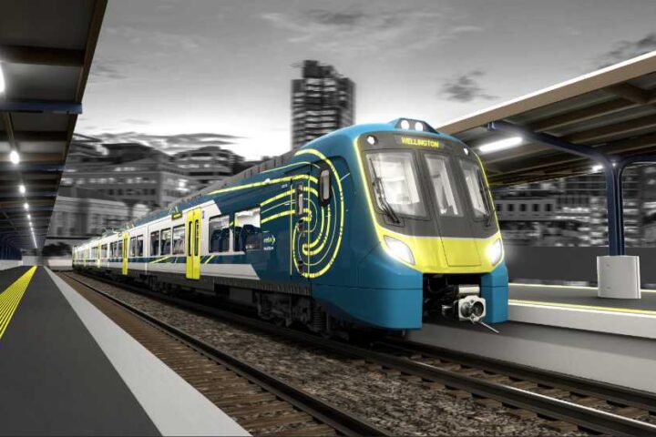 Modern blue and yellow Adessia Stream B battery-electric train with distinctive streamlined design at a station platform at night, showing the front cab and passenger cars with illuminated interior