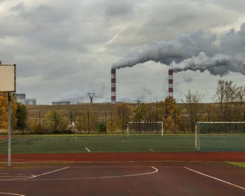 Basketball court and playing field at a school with industrial smokestacks emitting pollution visible in the background, demonstrating the proximity of pollution sources to community spaces in Kleszczow, Poland.