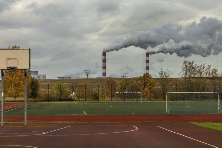 Basketball court and playing field at a school with industrial smokestacks emitting pollution visible in the background, demonstrating the proximity of pollution sources to community spaces in Kleszczow, Poland.
