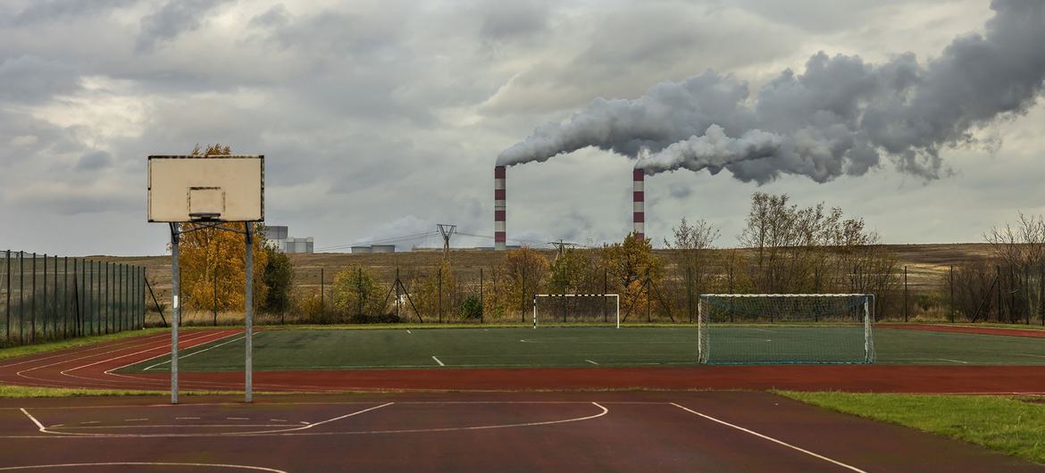 Basketball court and playing field at a school with industrial smokestacks emitting pollution visible in the background, demonstrating the proximity of pollution sources to community spaces in Kleszczow, Poland.