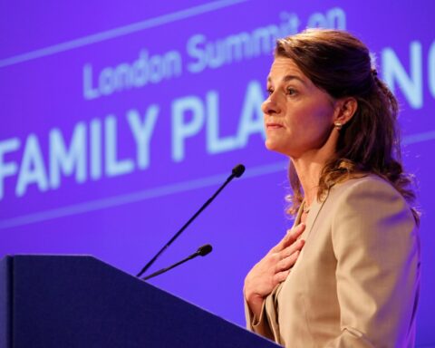 Melinda French Gates stands at a podium, speaking with her hand over her heart. Behind her, a purple screen displays the words 'London Summit on Family Planning'.