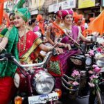 Women wearing colorful traditional Maharashtrian sarees and ornate jewelry riding decorated motorcycles with flowers during Gudi Padwa festival procession in Maharashtra, India.