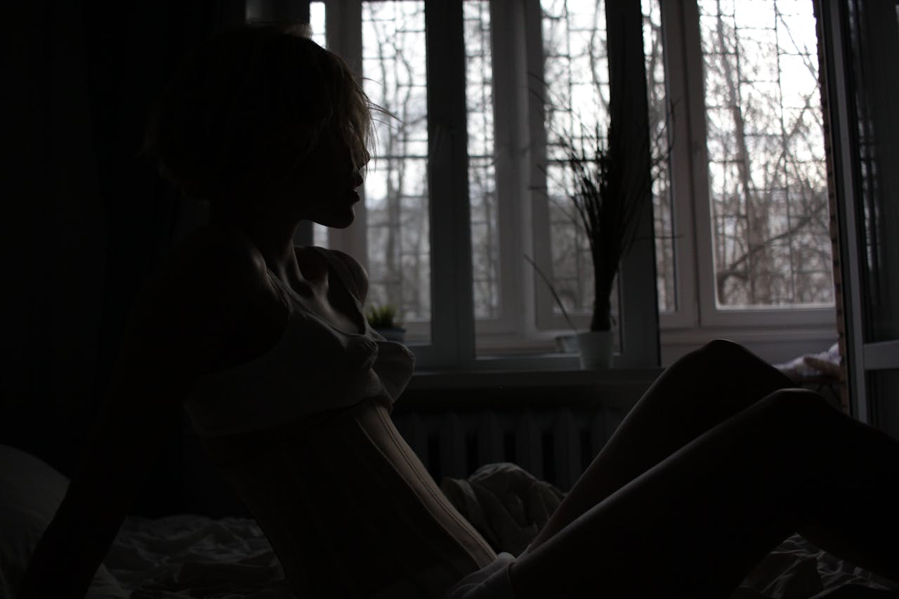 Representative Image. Silhouette of a person sitting alone by a window in dim lighting, conveying feelings of isolation and contemplation.