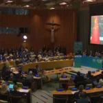 Chinese President Xi Jinping delivering a video address on screen at the United Nations Climate Summit with delegates seated in the General Assembly Hall watching.