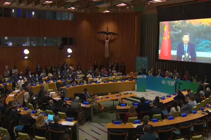 Chinese President Xi Jinping delivering a video address on screen at the United Nations Climate Summit with delegates seated in the General Assembly Hall watching.