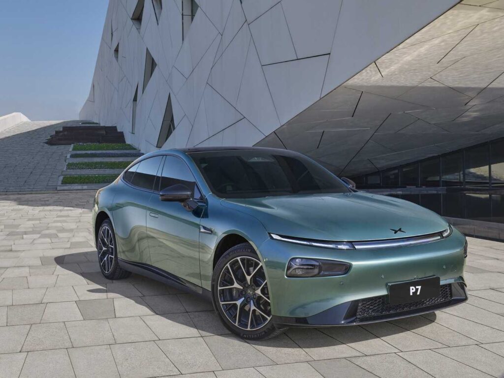Mint green Xpeng P7 electric sedan parked on light-colored stone pavement against a modern geometric white building background.