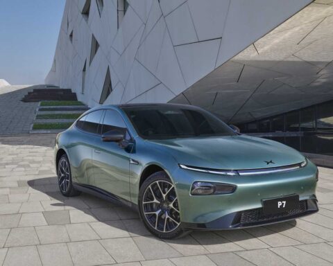 Mint green Xpeng P7 electric sedan parked on light-colored stone pavement against a modern geometric white building background.