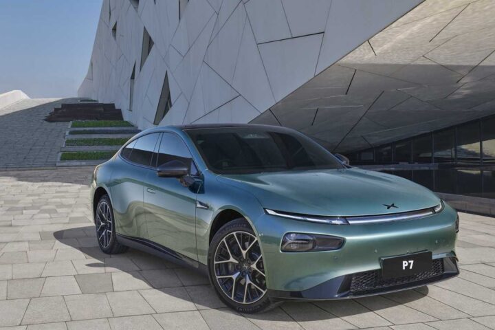 Mint green Xpeng P7 electric sedan parked on light-colored stone pavement against a modern geometric white building background.