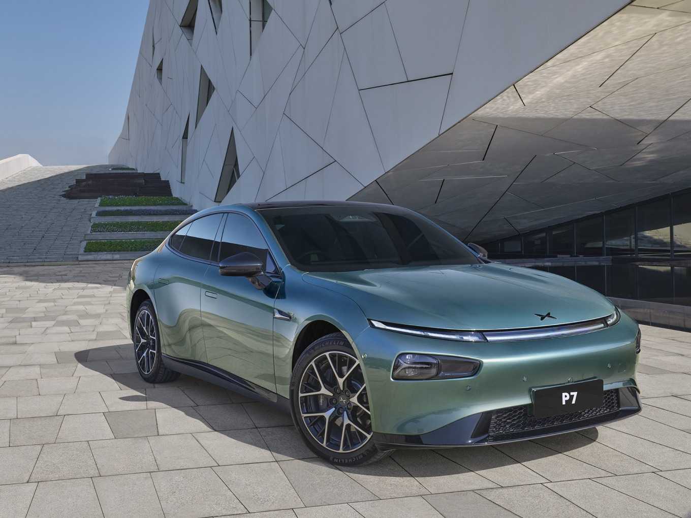 Mint green Xpeng P7 electric sedan parked on light-colored stone pavement against a modern geometric white building background.