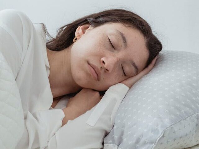 Woman sleeping peacefully in bed with white bedding next to a golden alarm clock on nightstand