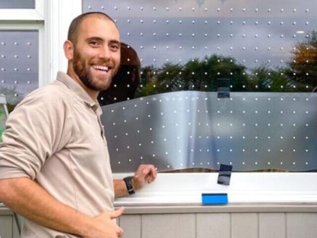 Two maintenance workers installing bird-safe window film with small dot patterns on windows at the Great Swamp National Wildlife Refuge Visitor Center in New Jersey.