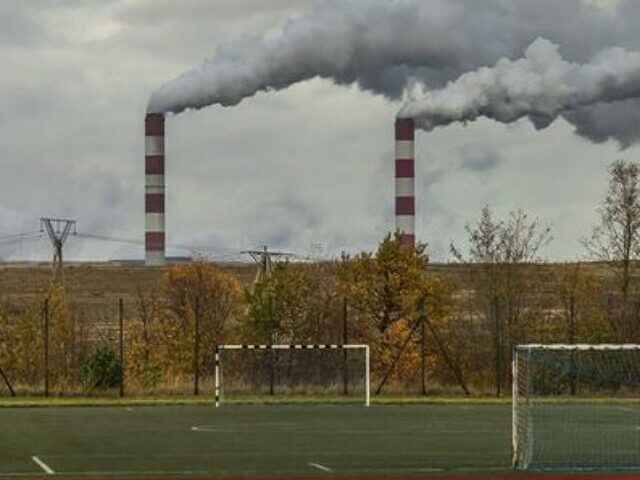 Basketball court and playing field at a school with industrial smokestacks emitting pollution visible in the background, demonstrating the proximity of pollution sources to community spaces in Kleszczow, Poland.