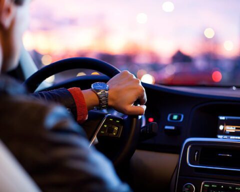 Person driving a car withds on the steering wheel, dashboard and city lights visible in the background