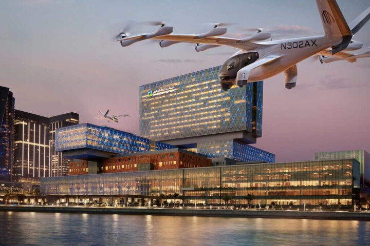 An Archer Midnight eVTOL aircraft flying over the Cleveland Clinic Abu Dhabi hospital at dusk, with the city skyline and water in the background.