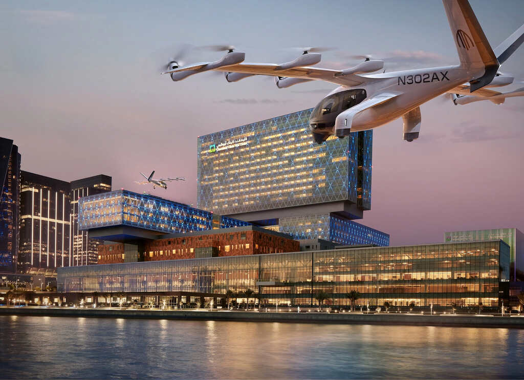 An Archer Midnight eVTOL aircraft flying over the Cleveland Clinic Abu Dhabi hospital at dusk, with the city skyline and water in the background.