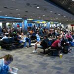 A crowded airport terminal with many passengers sitting and waiting, indicating flight delays.