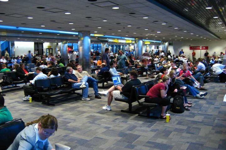 A crowded airport terminal with many passengers sitting and waiting, indicating flight delays.