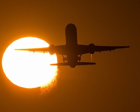 Airliner taking off against a blue sky, photographed from runway side with landing gear visible.