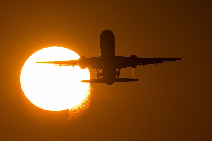 Airliner taking off against a blue sky, photographed from runway side with landing gear visible.