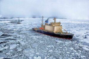 Research vessel navigating through fragmented sea ice in Antarctica, with broken ice floes surrounding the ship against a misty polar backdrop.